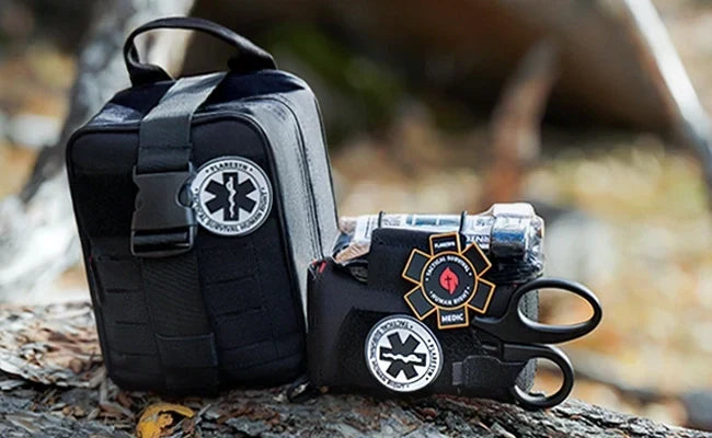 A waterproof wilderness trauma kit laid out on a rock beside a hiking backpack in a forest clearing