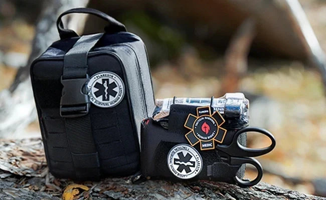 A waterproof wilderness trauma kit laid out on a rock beside a hiking backpack in a forest clearing